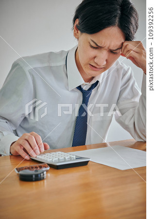 A young man making calculations on a calculator with a grimace on his face 109392256