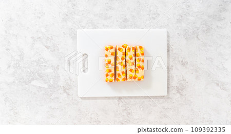 Flat lay. Cutting candy corn fudge into square pieces on a white cutting board. Flat lay. Cutting candy corn fudge into square pieces on a white cutting board. 109392335