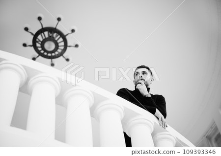 Thoughtful man on balcony overlooking classic interior 109393346