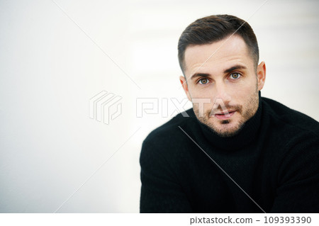 Close-up portrait of handsome young man wearing black turtleneck looking to camera over soft white background 109393390