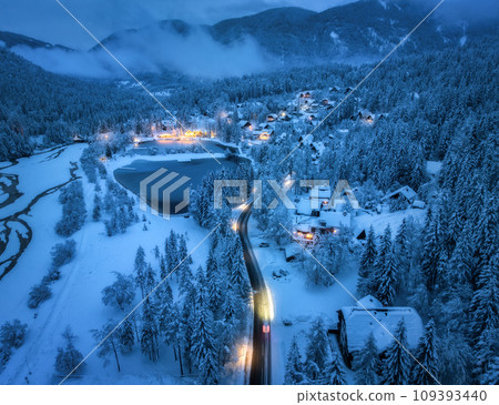Aerial view of snowy village, trees, lake, street lights at night Aerial view of snowy village, trees, lake, street lights at night 109393440