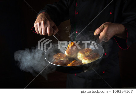 The chef is preparing oladki in a frying pan. The concept of preparing Ukrainian national dish or bliny in the kitchen. Black space for recipe or menu The chef is preparing oladki in a frying pan. The concept of preparing Ukrainian national dish or bliny in the kitchen. Black space for recipe or menu 109394167