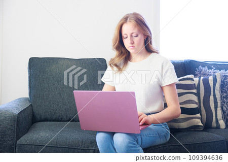 Caucasian woman sitting on a sofa and using a computer (calm) 109394636