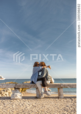 Couple in love is hugging and kissing while sitting bench on beach near ocean Couple in love is hugging and kissing while sitting bench on beach near ocean 109396692