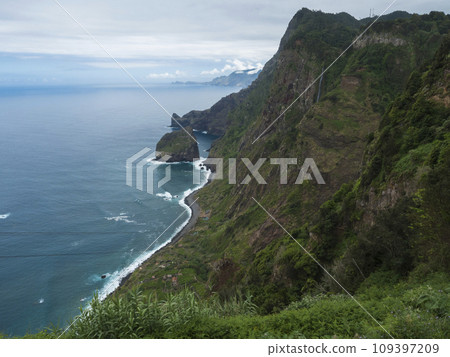 Scenic elevated view towards the Rocha do Navio Reserve and Ponta de Catarina Pires cape. Ocean, tropical green vegetation, cliffs and waterfall. Portugal, Madeira, Santana. 109397209