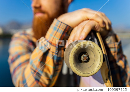 handsome redhaired man with long beard skateboarding near river at sunny summer day handsome redhaired man with long beard skateboarding near river at sunny summer day 109397525