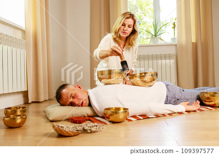 Woman playing on a tibetian singing bowl maling massage meditation for a man Woman playing on a tibetian singing bowl maling massage meditation for a man 109397577