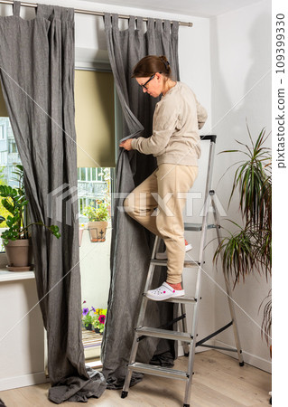 A woman hangs curtains A woman hangs curtains 109399330