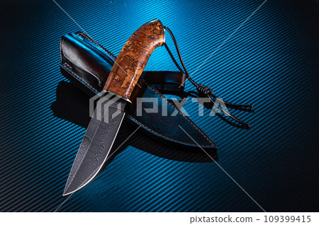 Hunting knife made of Damascus steel. Premium knife with leather sheath. Knife and leather lanyard. Carbon background with blue backlight.. 109399415
