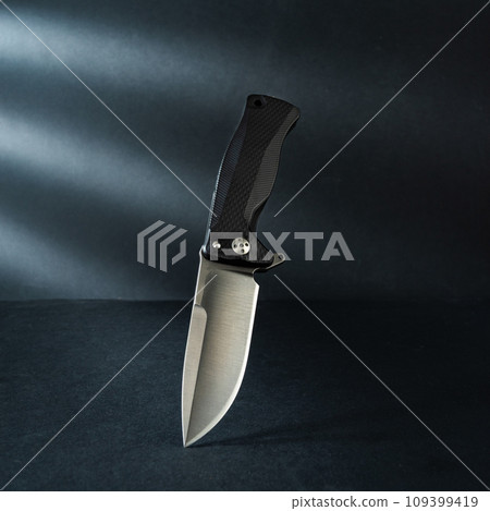 Beautiful photo of a knife. The knife stands vertically. Hard light from the window. Falling shadows on the background. Front view. 109399419