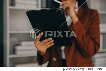 Attractive smiling young asian business woman work at home office, Asian woman working on laptop computer holding tablet. 109399985