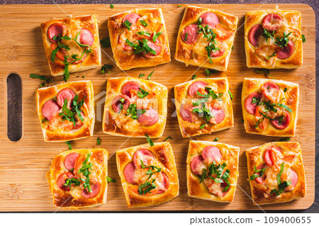 Close up of mini pizza with sausages, tomatoes, cheese and herbs on a wooden board top view 109400655