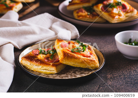Square mini pizza with tomato, sausage and cheese on a plate for a snack Square mini pizza with tomato, sausage and cheese on a plate for a snack 109400659