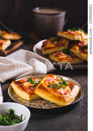 Square mini pizza with tomato, sausage and cheese on a plate for a snack vertical view Square mini pizza with tomato, sausage and cheese on a plate for a snack vertical view 109400662