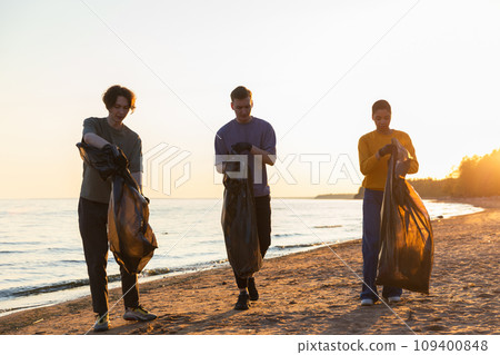 Earth day. Volunteers activists team collects garbage cleaning of beach coastal zone. Woman mans with trash in garbage bag on ocean shore. Environmental conservation coastal zone cleaning 109400848