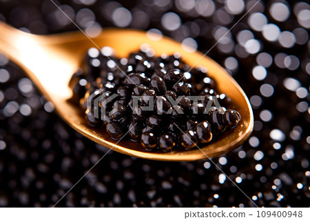 Closeup of natural black caviar on a golden spoon on black background, texture of fresh sturgeon caviar macro photo. 109400948