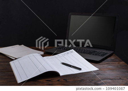 Financial notebook on the table and laptop nearby. Notebook and pen on the table. Maintaining records and finances. Planning and tasks. 109401087