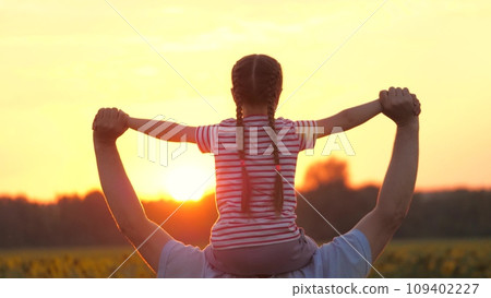 Father holds little daughter on shoulders showing field landscape with sunset 109402227