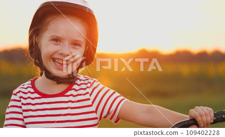 Young girl helmet-clad stands with laughter warming heart with sunset in field 109402228