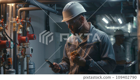 Professional engineer eats burger and uses phone at factory Professional engineer eats burger and uses phone at factory 109402790