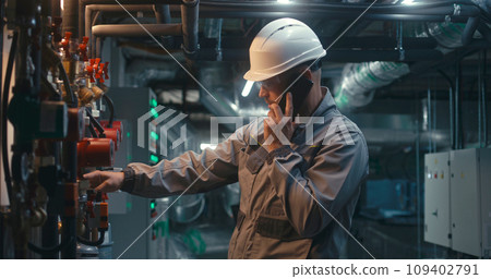 Heavy industry worker inspects pipeline system, talks by phone Heavy industry worker inspects pipeline system, talks by phone 109402791