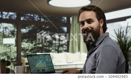 Business owner working on banking management at his modern mountain villa, looking at income trends. Self employed billionaire sitting at desk, hopping online to help his investment team. Business owner working on banking management at his modern mountain villa, looking at income trends. Self employed billionaire sitting at desk, hopping online to help his investment team. 109402985