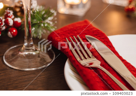 Christmas table setting. Plate and cutlery on napkin. Preparing for festive dinner. Candles burning on table on Christmas Eve. 109403023