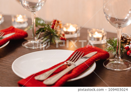 Christmas table setting. Plate and cutlery on napkin. Preparing for festive dinner. Candles burning on table on Christmas Eve. 109403024