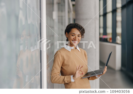 Stylish female freelancer working on laptop standing on coworking background and showing sign ok 109403056