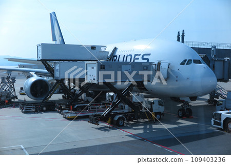 有多個食品裝載機正在將行李裝載到兩層空中巴士 A380 飛機上（窗玻璃的反射） 109403236