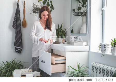 Happy young woman standing near dressing table and taking out a beauty cosmetic from drawer. Happy young woman standing near dressing table and taking out a beauty cosmetic from drawer. 109403483