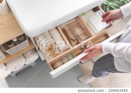 Top view of woman hands neatly organizing bathroom amenities and toiletries in drawer in bathroom. 109403485