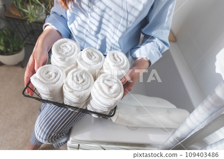 Woman's hands neatly putting or displaying a clean rolled up white towels made from organic cotton. 109403486