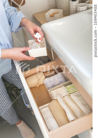 Top view of woman hands neatly organizing bathroom amenities and toiletries in drawer in bathroom. 109403488