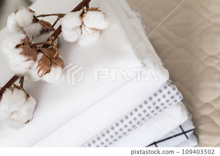 Cotton branch with pile of folded bed sheets and blankets 109403502