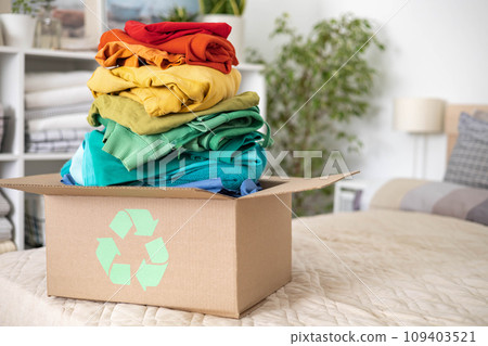 A stack of clothes in different colors in a box with a recycle sign. A stack of clothes in different colors in a box with a recycle sign. 109403521