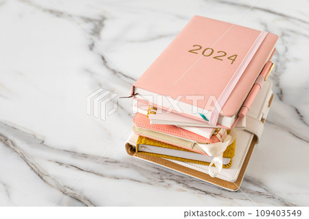 Pink coral colored diary for the year 2024 and many other diaries, pen, marble background Pink coral colored diary for the year 2024 and many other diaries, pen, marble background 109403549