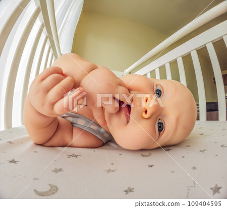 A playful baby in the crib, gleefully staring at the camera, radiating joy A playful baby in the crib, gleefully staring at the camera, radiating joy 109404595