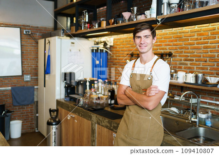 Professional young coffee barista standing inside the counter bar in the coffee shop and making arms crossed and looking at camera, handsome - good looking caucasian ethnic barista posing. 109410807