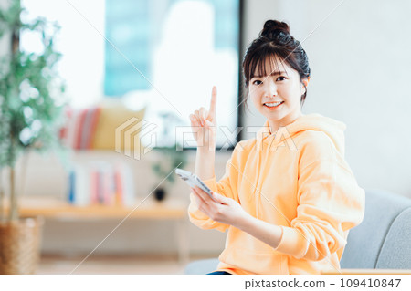 A young woman operating a smartphone in the living room. 109410847