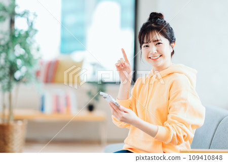 一位年輕女子在客廳操作智慧型手機。 一位年輕女子在客廳操作智慧型手機。 109410848