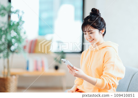 A young woman operating a smartphone in the living room. A young woman operating a smartphone in the living room. 109410851