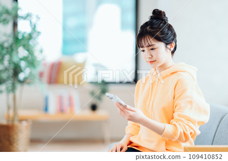 A young woman operating a smartphone in the living room. A young woman operating a smartphone in the living room. 109410852