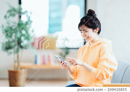 A young woman operating a smartphone in the living room. A young woman operating a smartphone in the living room. 109410855