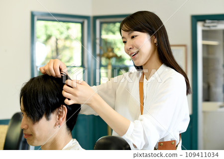 Asian female hairdresser styling a male customer's hair Asian female hairdresser styling a male customer's hair 109411034