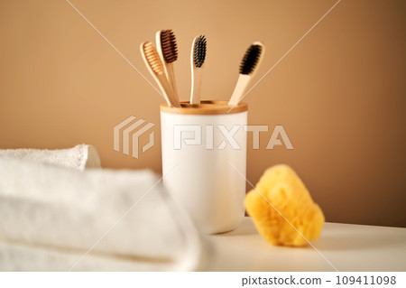 Bamboo toothbrushes in a cup and a towel in a bathroom interior. Bamboo toothbrushes in a cup and a towel in a bathroom interior. 109411098