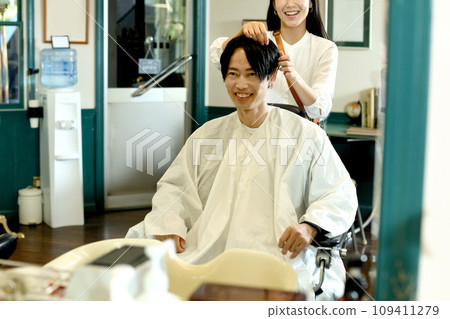 Asian female hairdresser cutting the hair of a male customer 109411279