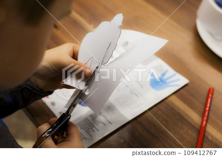 A child cuts paper with scissors, carves figures of knights while sitting at a table. 109412767