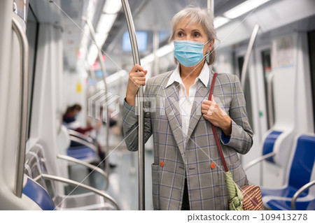 Senior lady in mask standing in metro train 109413278