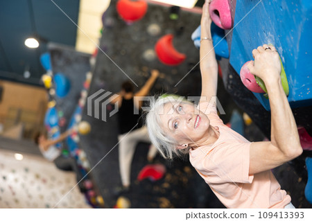 Mature female fitness climber training at bouldering gym.Woman rise up on artificial climbing wall Mature female fitness climber training at bouldering gym.Woman rise up on artificial climbing wall 109413393